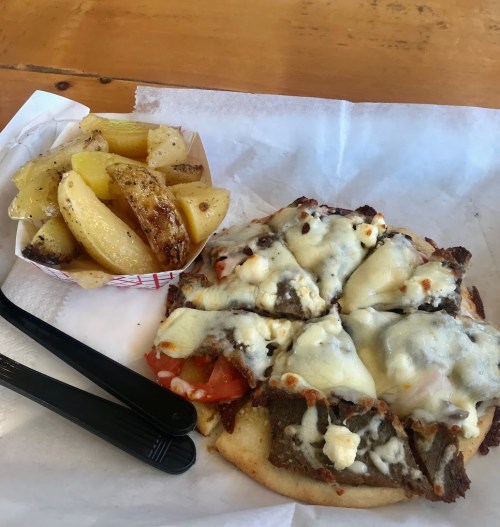 A plate featuring a slice of pizza topped with meat and cheese, alongside a serving of seasoned potato wedges.