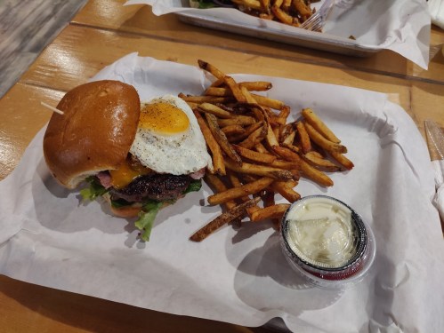 A juicy burger with a fried egg, lettuce, and cheese, served with crispy fries and a side of dipping sauce.