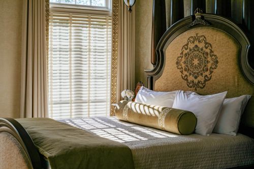 Cozy bedroom with a large bed, decorative headboard, and sunlight streaming through blinds.
