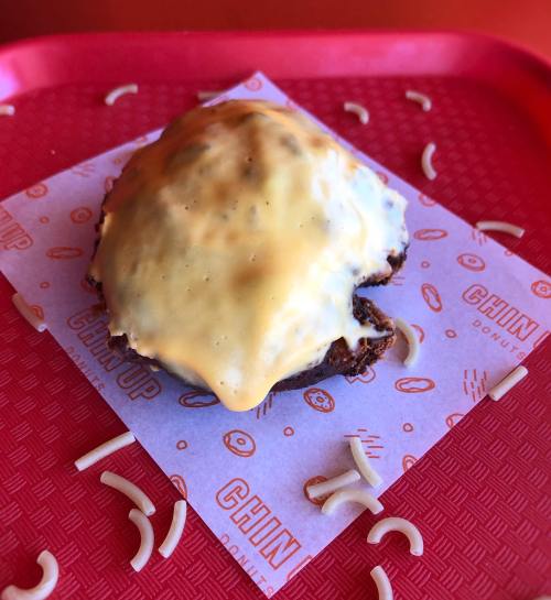 A donut topped with melted cheese on a red tray, surrounded by small pasta shapes.