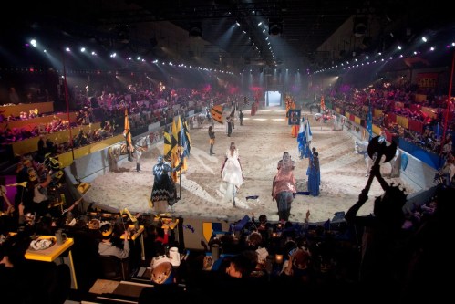A medieval-themed arena with knights, horses, and a cheering crowd, set for a jousting tournament.