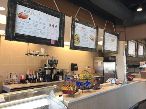 A café counter with menus hanging above, featuring desserts and snacks, and a display of ice cream and toppings.