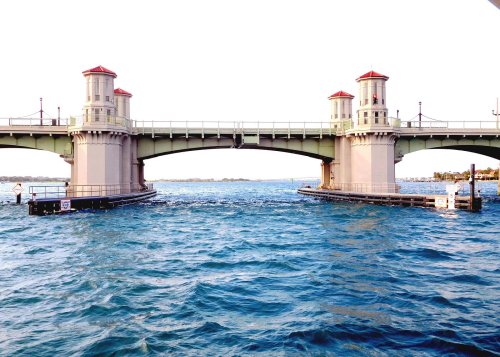 A bridge with two towers spans over a body of water, with waves gently rippling beneath it.