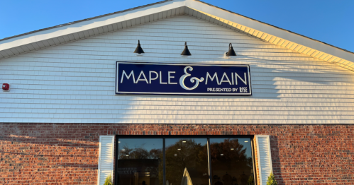 Sign for "Maple & Main" on a brick building with a white exterior and large windows.