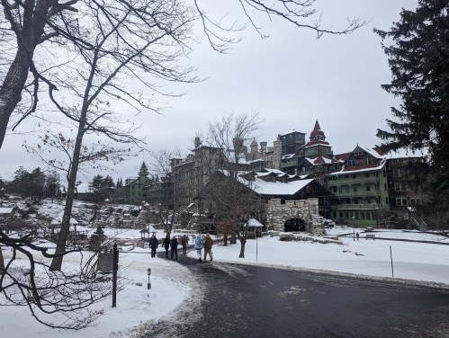 A snowy landscape featuring a large historic hotel with green and red architecture, surrounded by bare trees.