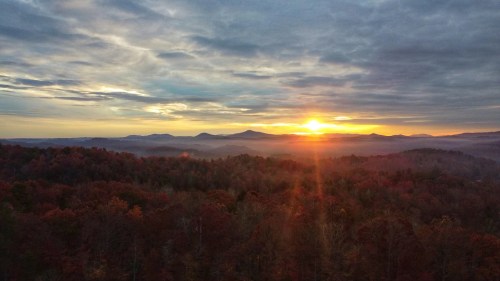 A stunning sunset over rolling hills, with vibrant autumn foliage and a cloudy sky.