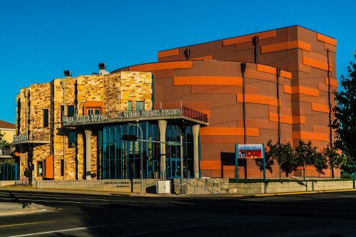 Modern building with a mix of stone and orange paneling, featuring large windows and a welcoming entrance.