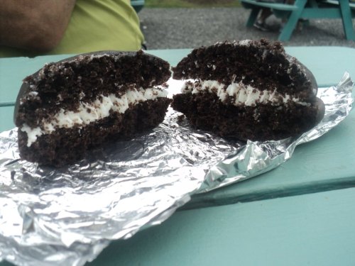 A chocolate whoopie pie cut in half, revealing a creamy filling, resting on silver foil on a teal table.