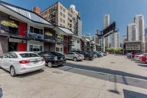 A parking lot with several cars in front of a multi-story building featuring balconies and a sign for Ohio House.