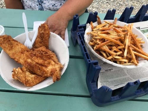 A plate of fried fish fillets next to a bowl of crispy French fries on a table.