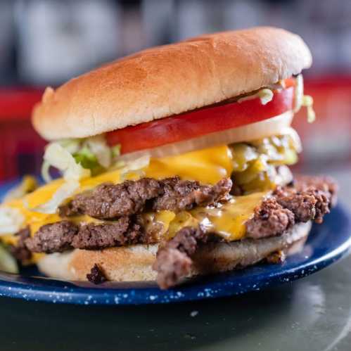 A close-up of a juicy cheeseburger with two beef patties, melted cheese, lettuce, tomato, and pickles on a soft bun.