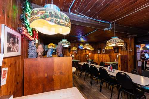 Cozy restaurant interior with wooden walls, colorful lamps, and empty tables set for dining.