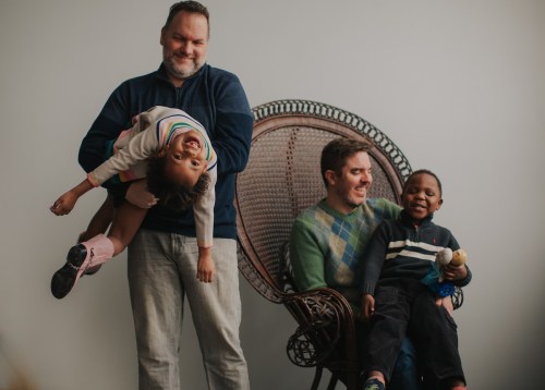 A joyful family portrait with two men and two children, one child playfully hanging upside down.