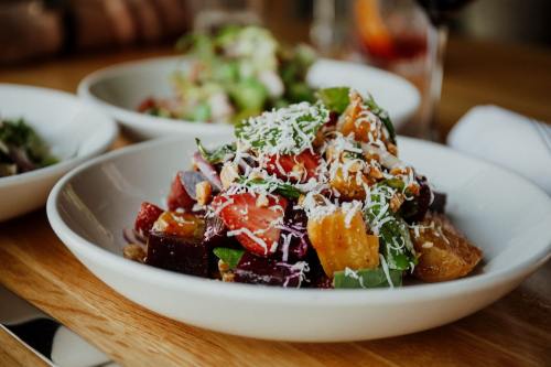 A colorful salad with beets, greens, and shredded cheese served in a white bowl on a wooden table.