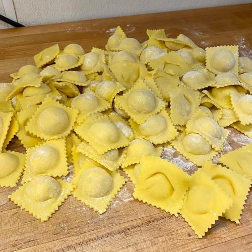 A pile of freshly made ravioli on a wooden surface, dusted with flour.