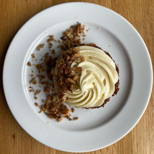 A beautifully swirled cupcake topped with cream cheese frosting and sprinkled with crushed nuts on a white plate.