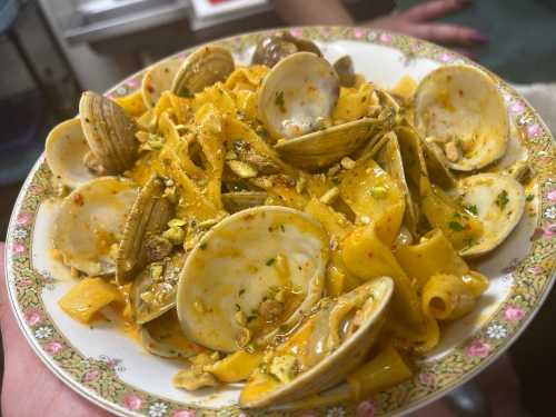 A plate of pasta with clams, garnished with herbs and crushed pistachios, served in a decorative dish.