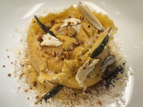 A beautifully plated dish of pasta topped with herbs, nuts, and cheese, garnished with delicate slices.