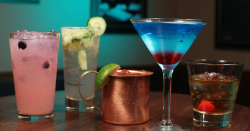 a wood table with a selection of cocktails including a martini in a peacock alley martini glass