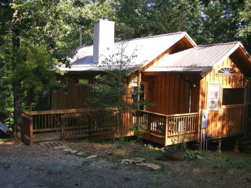 A cozy wooden cabin surrounded by trees, featuring a porch and a chimney, set in a natural landscape.