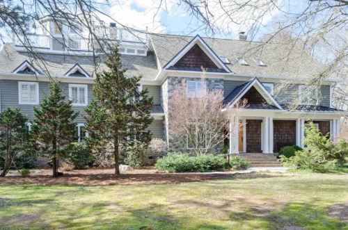 A large, elegant house with a mix of stone and siding, surrounded by trees and a well-maintained lawn.