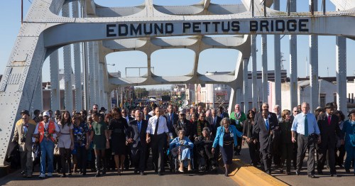 A diverse group of people marches across the Edmund Pettus Bridge, symbolizing unity and civil rights.
