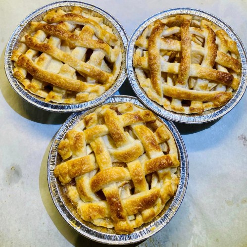 Three freshly baked apple pies with golden lattice crusts, arranged on a light surface.