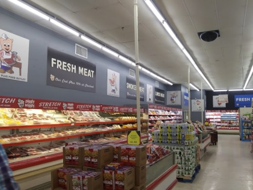A grocery store aisle featuring fresh meat displays, signage for smoked meat, and various packaged goods on shelves.