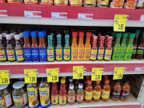 A colorful display of various hot sauces and condiments on a grocery store shelf, with price tags visible.