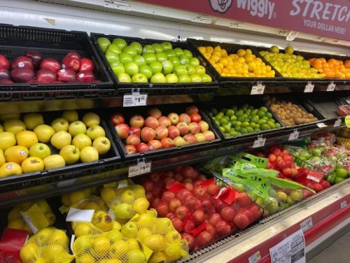 A colorful display of various fruits, including apples, oranges, lemons, and limes, arranged in grocery store bins.