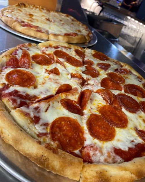 Two pizzas on metal trays, one topped with pepperoni and melted cheese, showcasing a golden crust.