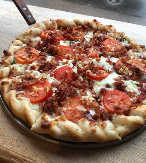 A freshly baked pizza topped with tomatoes, bacon, and cheese on a wooden surface.