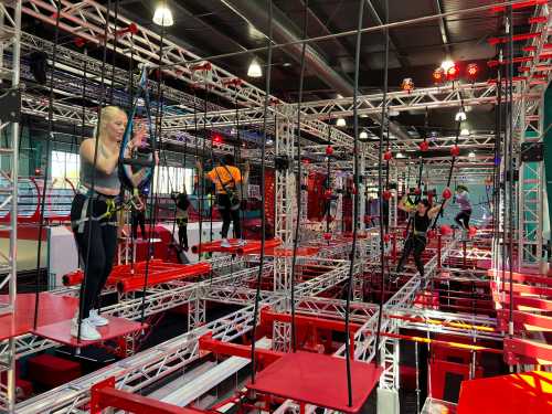 A group of people navigating an indoor obstacle course with ropes and platforms, surrounded by bright lights.