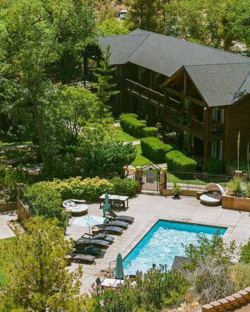 Aerial view of a lodge with a pool, surrounded by greenery and lounge chairs, in a serene outdoor setting.