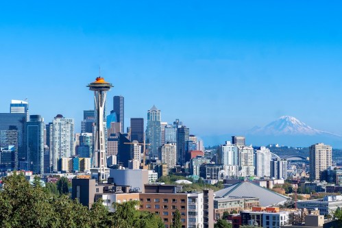 Seattle skyline featuring the Space Needle, with Mount Rainier in the background under a clear blue sky.