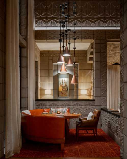 Cozy dining area with a round orange table, leather chairs, and decorative wall features, illuminated by pendant lights.