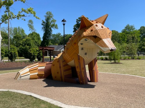 A large wooden fox sculpture in a park, made from various colored wooden planks, under a clear blue sky.