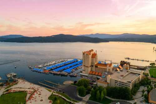 Aerial view of a marina at sunset, featuring boats, a hotel, and mountains in the background.