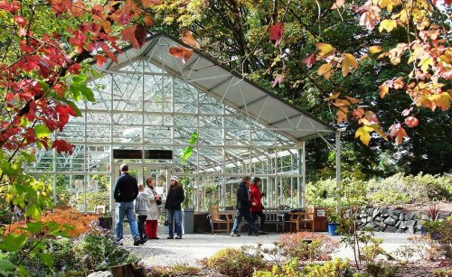 A glass greenhouse surrounded by colorful autumn foliage, with people gathered outside.