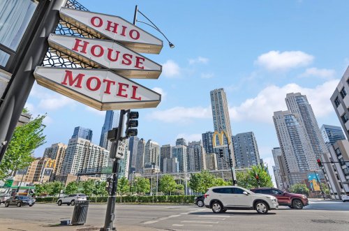 Sign for Ohio House Motel with city skyline and McDonald's in the background on a sunny day.