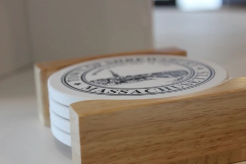 A set of white coasters in a wooden holder, featuring a design related to Massachusetts.