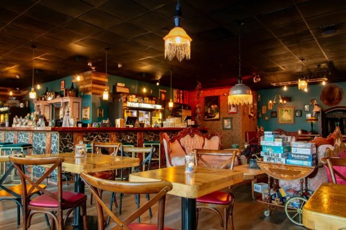 Cozy restaurant interior with wooden tables, colorful decor, and warm lighting, featuring a bar and vintage furnishings.