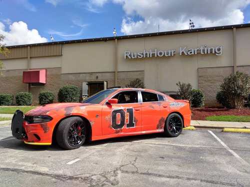 An orange car with the number 01 parked outside RushHour Karting, featuring a damaged exterior and black wheels.