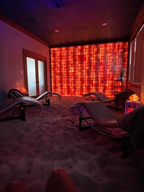 A tranquil spa room with lounge chairs, a sandy floor, and a glowing wall of salt lamps, creating a relaxing atmosphere.