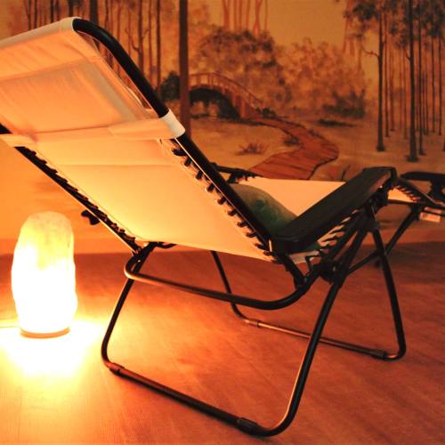 A reclining chair next to a glowing salt lamp, set against a mural of a serene landscape.