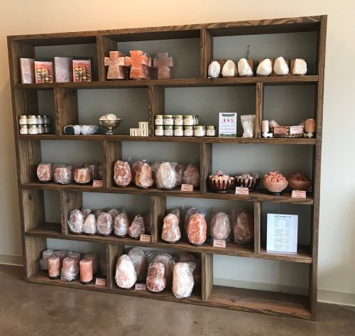 A wooden shelf displaying various salt products, including lamps, blocks, and jars, organized neatly.