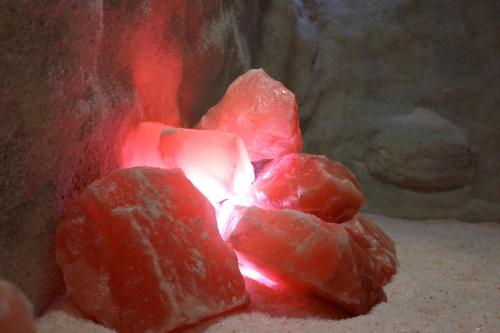 Glowing pink salt crystals arranged on a sandy surface, illuminated by soft red light against a rocky background.