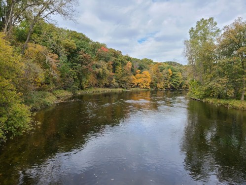 A serene river surrounded by trees displaying autumn colors under a cloudy sky.