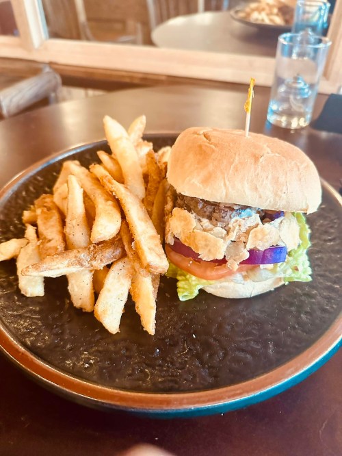 A plate with a burger topped with lettuce, tomato, and crispy onion, served with a side of golden fries.