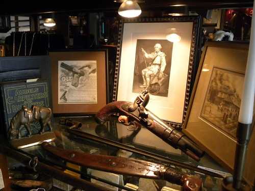 A display of vintage items, including a pistol, photographs, and decorative objects, arranged on a wooden surface.